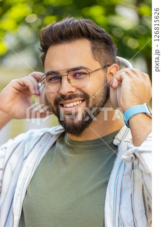 Caucasian young man taking off wireless headphones looking at camera and smiling on city street 126815626