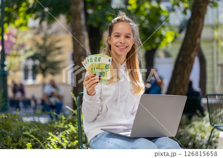 Happy rich woman using laptop winner victory holding cash money in euro banknotes sitting on chair 126815658