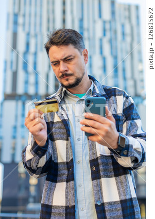 Frustrated mature businessman using credit card and mobile phone standing on downtown city street 126815672