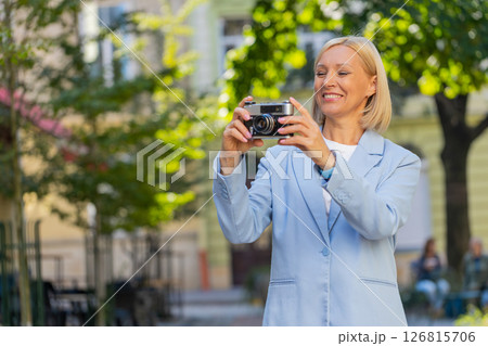 Happy mature businesswoman using vintage camera to take photos of fascinating city on street Happy mature businesswoman using vintage camera to take photos of fascinating city on street 126815706