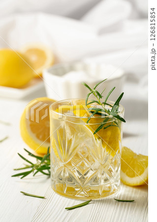 Summer refreshing lemonade drink or alcoholic cocktail with ice, rosemary and lemon slices on the white table. Summer refreshing lemonade drink or alcoholic cocktail with ice, rosemary and lemon slices on the white table. 126815854