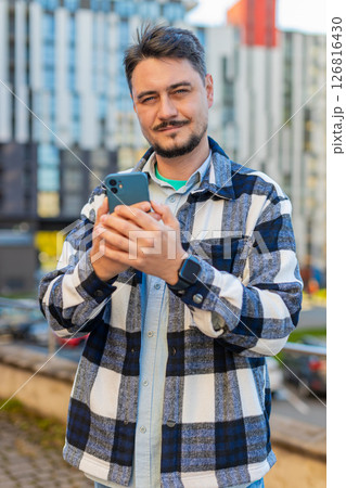 Happy mature man tourist using smartphone and looking at camera while standing in downtown street Happy mature man tourist using smartphone and looking at camera while standing in downtown street 126816430