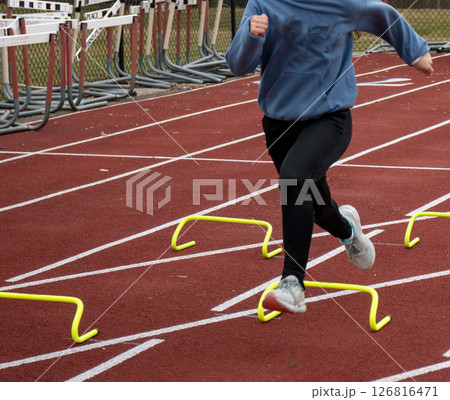 Runner Training With Mini Hurdles on a Red Track Field During Practice Runner Training With Mini Hurdles on a Red Track Field During Practice 126816471