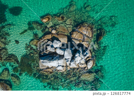 Rugged coastal rock formation emerging from clear turquoise waters in a serene seaside location Rugged coastal rock formation emerging from clear turquoise waters in a serene seaside location 126817774