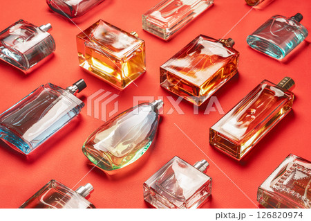 An elegant display features a diverse collection of glass perfume and cologne bottles, each uniquely shaped and filled with various fragrances. The bottles are arranged on a vivid red background, An elegant display features a diverse collection of glass perfume and cologne bottles, each uniquely shaped and filled with various fragrances. The bottles are arranged on a vivid red background, 126820974