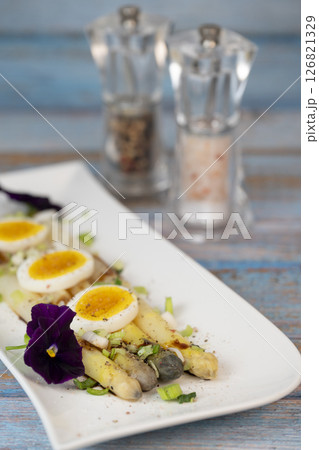 Baked asparagus with boiled egg in big white plate on blue background Baked asparagus with boiled egg in big white plate on blue background 126821329