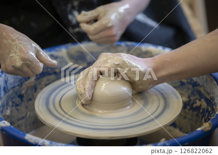 The potter teaches the craft to the child. Close-up of a potter's hands and a child's hand with a product on a potter's wheel. Working with clay. Clay master class. The potter teaches the craft to the child. Close-up of a potter's hands and a child's hand with a product on a potter's wheel. Working with clay. Clay master class. 126822062