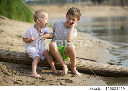 Two brothers, the elder and the younger, are playing by the river. Children on the sandy shore talk and indulge. Two brothers, the elder and the younger, are playing by the river. Children on the sandy shore talk and indulge. 126823439
