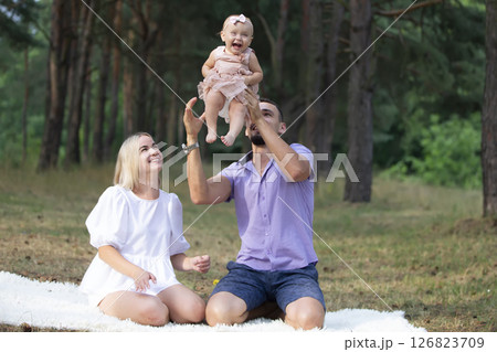 Husband, wife and their little daughter for a walk in the park. Happy dad and mom toss up their little daughter. 126823709