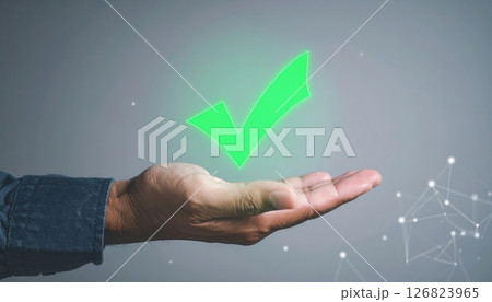 Hand holding a glowing green checkmark over a gray background representing approval or success concept 126823965