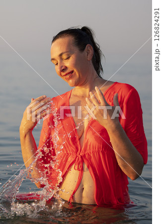 Beautiful elderly woman bathes in the sea and splashes water. 126824291