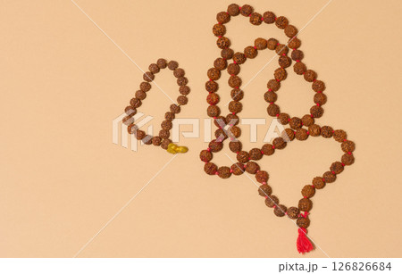 Top view of two strands of rudraksha beads, one of which is longer and has a red tassel, placed on a beige background Top view of two strands of rudraksha beads, one of which is longer and has a red tassel, placed on a beige background 126826684