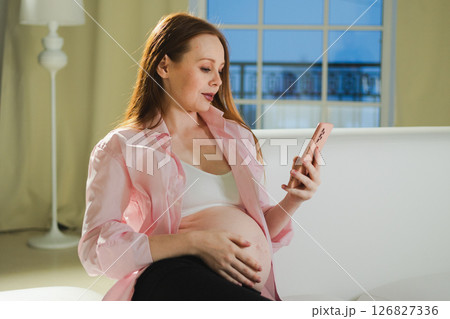 Pregnancy motherhood. Pregnant woman with smartphone typing scrolling at home. Woman with cell phone enjoying pregnancy surfing internet using social media apps. Mobile application for pregnant women 126827336