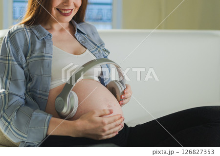 Pregnancy motherhood. Pregnant woman holding headphones near belly listening music for mother and unborn baby. Girl enjoying pregnancy listen music for relax calm wellness. Prenatal music stimulation Pregnancy motherhood. Pregnant woman holding headphones near belly listening music for mother and unborn baby. Girl enjoying pregnancy listen music for relax calm wellness. Prenatal music stimulation 126827353