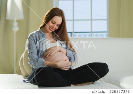 Pregnancy motherhood people expectation future. Pregnant woman touching big belly sitting on couch at home. Girl hugging her tummy enjoying pregnancy. Maternity tenderness parenthood new life concept 126827378