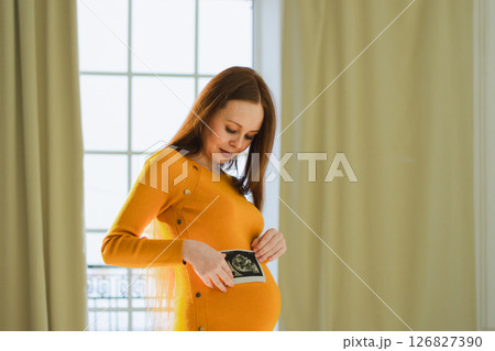 Prenatal ultrasound screening. Pregnant woman holding sonogram picture of unborn baby inside her big belly. Happy expectant mom with fetus usi scan image. Young mother enjoying pregnancy. Maternity Prenatal ultrasound screening. Pregnant woman holding sonogram picture of unborn baby inside her big belly. Happy expectant mom with fetus usi scan image. Young mother enjoying pregnancy. Maternity 126827390