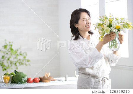 キッチンで花瓶を持つ笑顔のミドル女性 キッチンで花瓶を持つ笑顔のミドル女性 126829210