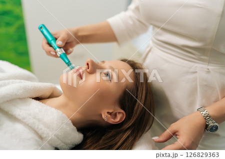 Closeup face of pretty female patient receiving rejuvenation treatment in cosmetology clinic. Professional beautician performing mesotherapy treatment to woman focusing on skin rejuvenation, hydration Closeup face of pretty female patient receiving rejuvenation treatment in cosmetology clinic. Professional beautician performing mesotherapy treatment to woman focusing on skin rejuvenation, hydration 126829363