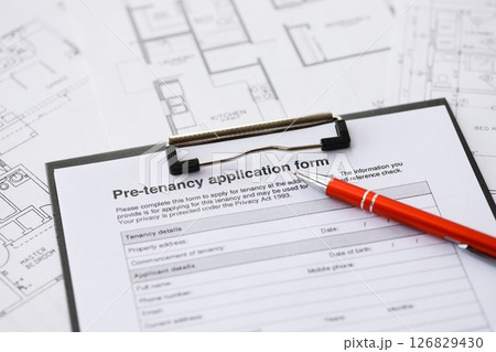 Pen on pre-tenancy application form and planning blueprints of residential building project close up 126829430