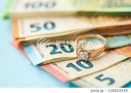 European union Euro money bills and coins with golden wedding ring on blue table European union Euro money bills and coins with golden wedding ring on blue table 126829436