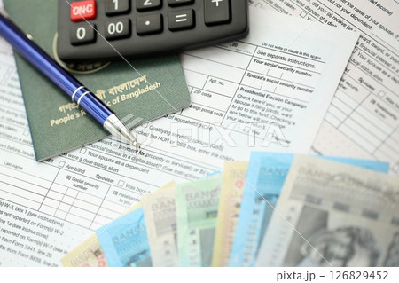 Bangladeshi taka money bills lies on table with pen, calculator, passport and tax forms 126829452