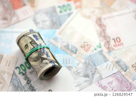 Roll of US dollar bills lies on big amount of Brazilian reais banknotes close up 126829547