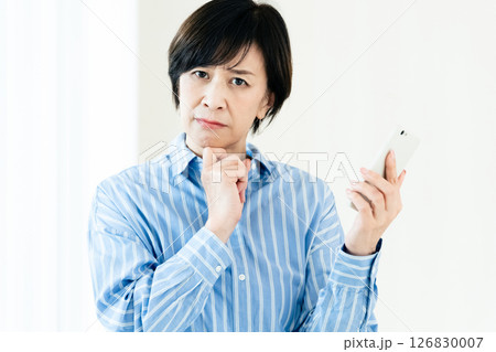 スマホを持って悩む中高年女性 スマホを持って悩む中高年女性 126830007
