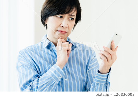 スマホを持って悩む中高年女性 126830008