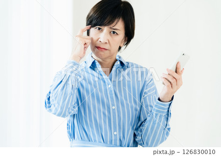 スマホを持って悩む中高年女性 スマホを持って悩む中高年女性 126830010