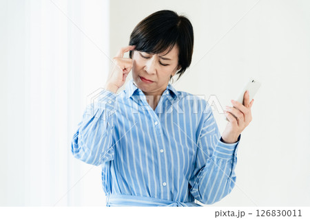 スマホを持って悩む中高年女性 126830011