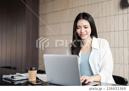 Smiling young woman working on a laptop at a stylish cafe, showcasing modern work-life balance. 126831369