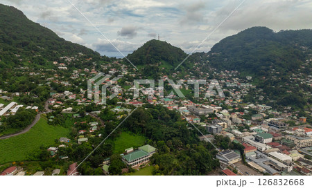 Dense residential area nestled between green hills with lush vegetation, various buildings, and winding roads visible. Seychelles, Mahe. Dense residential area nestled between green hills with lush vegetation, various buildings, and winding roads visible. Seychelles, Mahe. 126832668