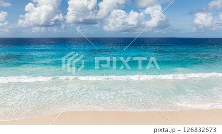 Turquoise waters and waves crashing onto a wide sandy beach. La Digue, Seychelles. 126832673