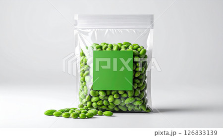 Clear plastic bag filled with green edamame beans, some spilling out, on white background 126833139