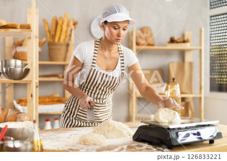 Woman in bakery cutting dough and weighing Woman in bakery cutting dough and weighing 126833221