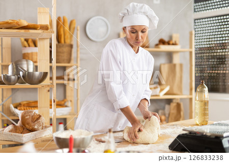 Working in bakery - woman kneads raw dough to make baguettes or croissants Working in bakery - woman kneads raw dough to make baguettes or croissants 126833238