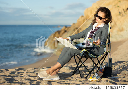 Businesswoman working on laptop and drinking whiskey on seashore. Remote work concept Businesswoman working on laptop and drinking whiskey on seashore. Remote work concept 126833257
