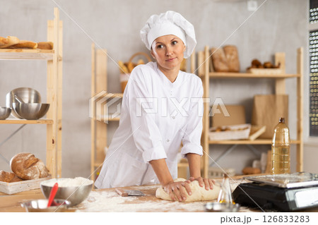 Adult female baker kneading dough on table 126833283