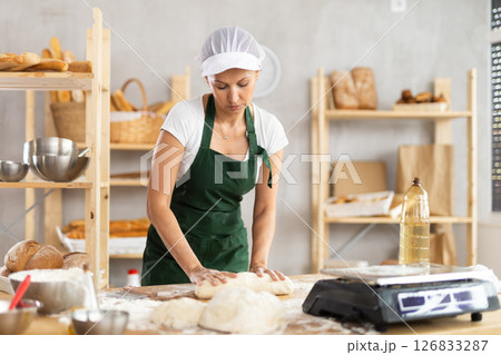 Woman works as baker, mold baguette from dough, creates long loafs from dough. 126833287