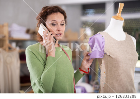 Woman seamstress talks on phone in workshop 126833289