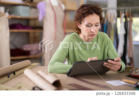 Woman tailor creates sketch of dress on tablet Woman tailor creates sketch of dress on tablet 126833306