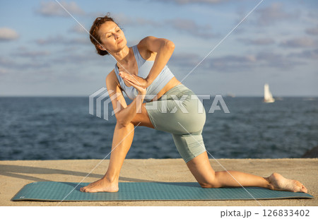 Yoga practice on embankment, female athlete fulfil carry out parivritta Anjaneyasana 126833402