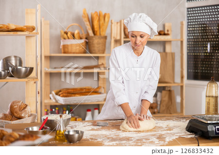 Middle-aged woman baker kneads the dough in bakery 126833432
