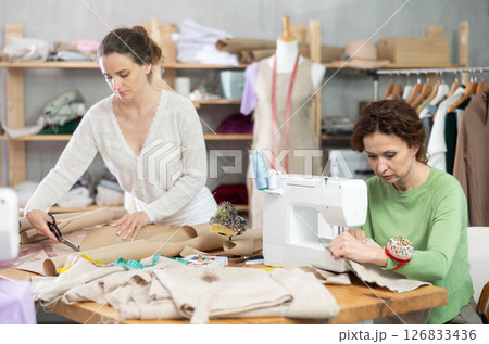 Woman tailor at work in cloth design shop. Apprentice cut out paper dress pattern 126833436