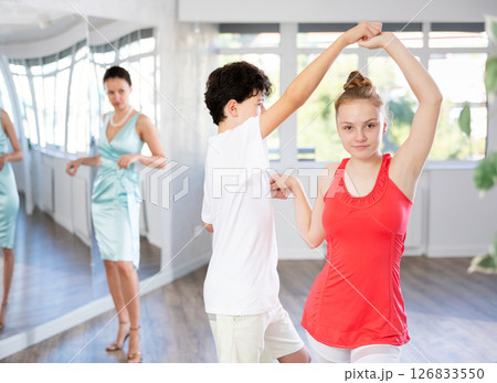 Experienced dance teacher teaching ballroom dancing to a couple of teenagers in studio Experienced dance teacher teaching ballroom dancing to a couple of teenagers in studio 126833550