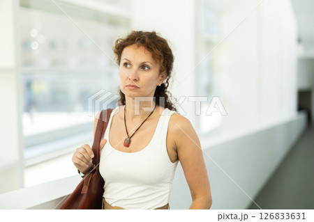Woman with curly brown hair walking through bright hallway 126833631