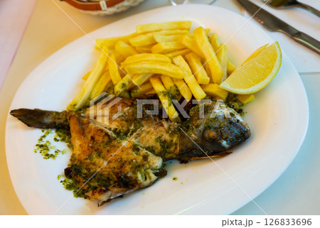 Baked in oven dorado fish with lemon and french fries served Baked in oven dorado fish with lemon and french fries served 126833696