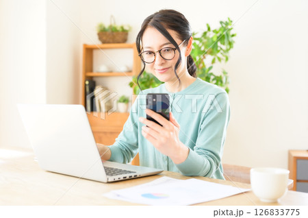 スマホを片手にパソコンで仕事中のミドル女性 スマホを片手にパソコンで仕事中のミドル女性 126833775