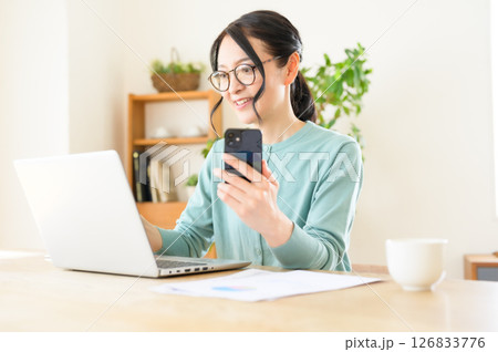 スマホを片手にパソコンで仕事中のミドル女性 126833776