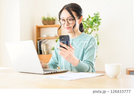 スマホを片手にパソコンで仕事中のミドル女性 スマホを片手にパソコンで仕事中のミドル女性 126833777